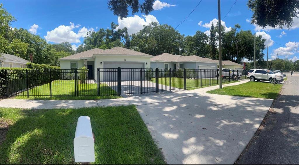 A fenced front yard with a concrete driveway and two single-story houses under a blue sky — 1226 36TH STREET, ORLANDO, FL