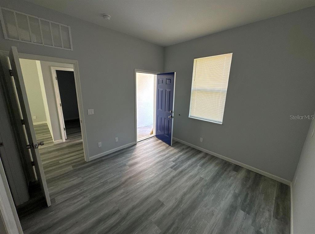 An empty room features light gray walls, wood-look flooring, a window with blinds, and a door — 1226 36TH STREET, ORLANDO, FL