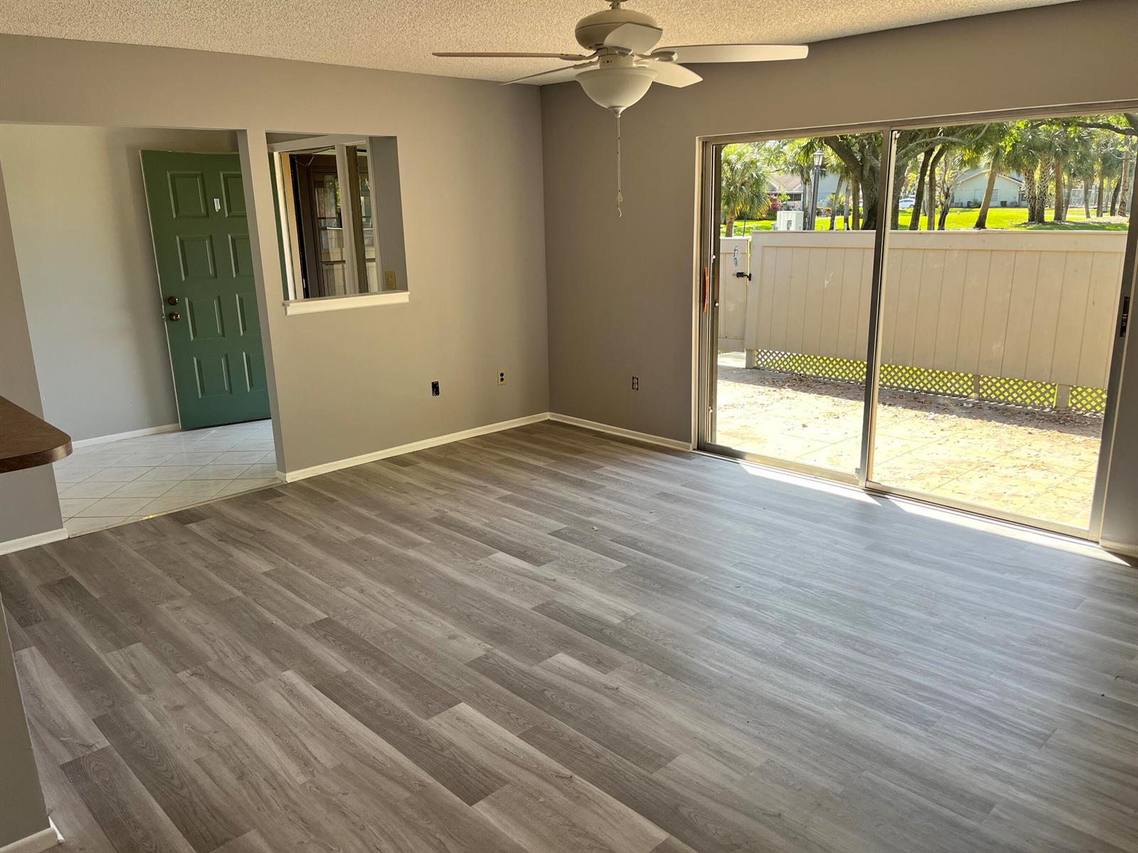 An empty living room with gray walls, wood-look flooring, a ceiling fan, and sliding glass doors — 4116 NW Cinnamon Tree Circle, Jensen Beach FL 34957, JENSEN BEACH, FL