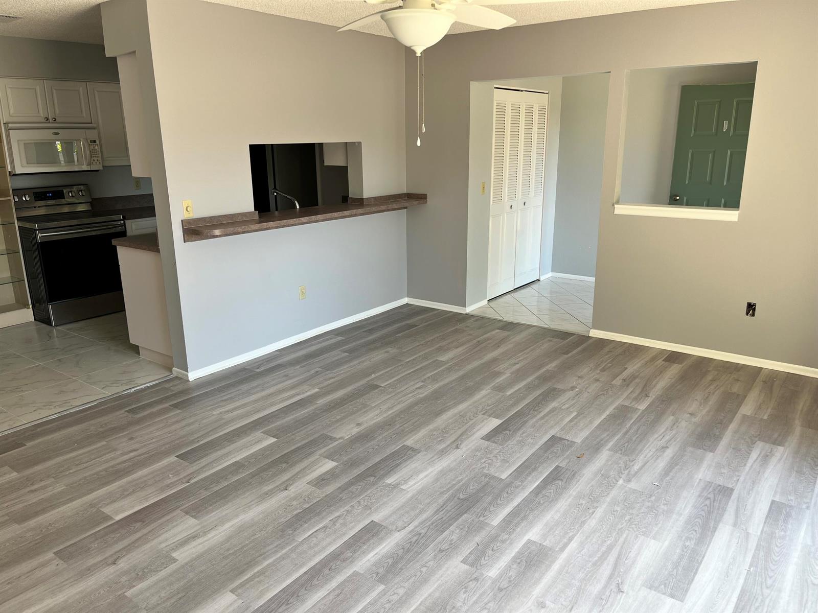 An open living area features gray walls, wood-look flooring, a kitchen pass-through, and ceiling fan — 4116 NW Cinnamon Tree Circle, Jensen Beach FL 34957, JENSEN BEACH, FL