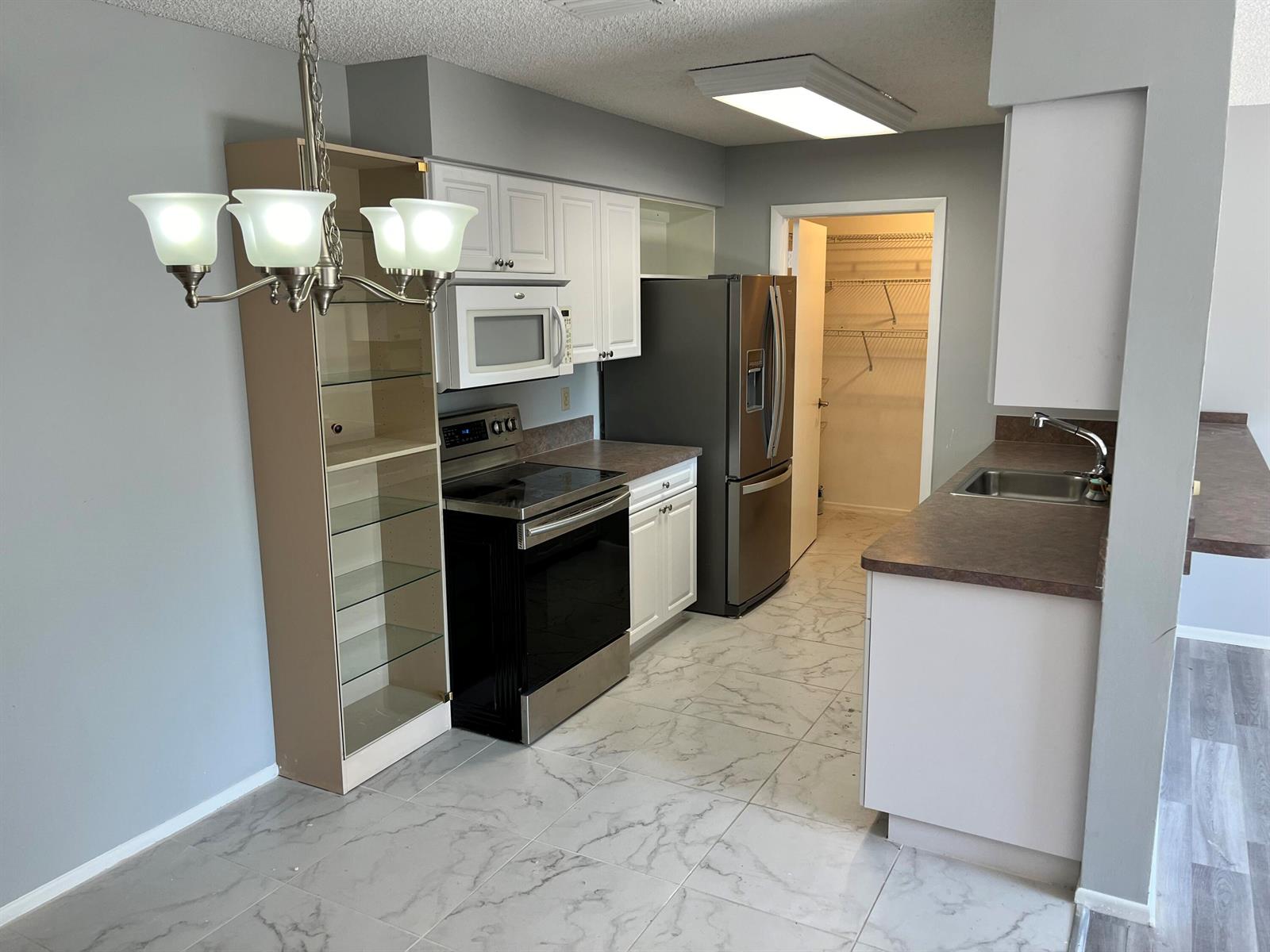 A kitchen features white cabinets, stainless steel appliances, a pantry, and light-colored marble-patterned tile flooring — 4116 NW Cinnamon Tree Circle, Jensen Beach FL 34957, JENSEN BEACH, FL