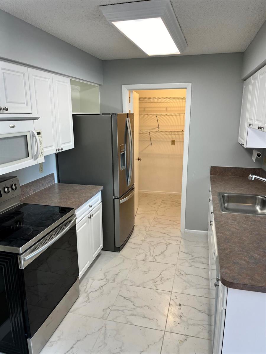 A kitchen features white cabinets, dark countertops, stainless steel appliances, and light marble-patterned tile floors — 4116 NW Cinnamon Tree Circle, Jensen Beach FL 34957, JENSEN BEACH, FL