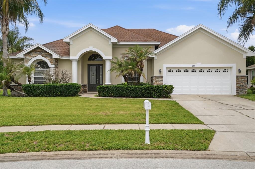 A single-story house with a beige stucco exterior, stone accents, and a two-car garage — 200 LAKE ARIETTA COURT, AUBURNDALE, FL