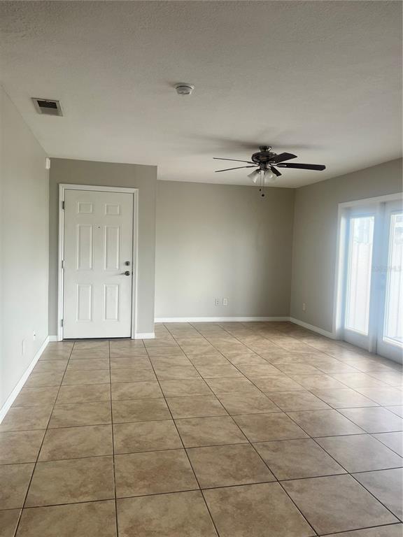 An empty room features beige tile flooring, a ceiling fan, a white door, and glass doors — 4728 BEACH DRIVE SE UNIT B, ST PETERSBURG, FL