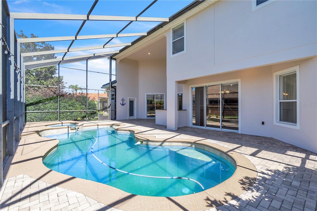 A screened-in patio features a swimming pool, a hot tub, and a paved deck — 11538 DELWICK DRIVE, WINDERMERE, FL