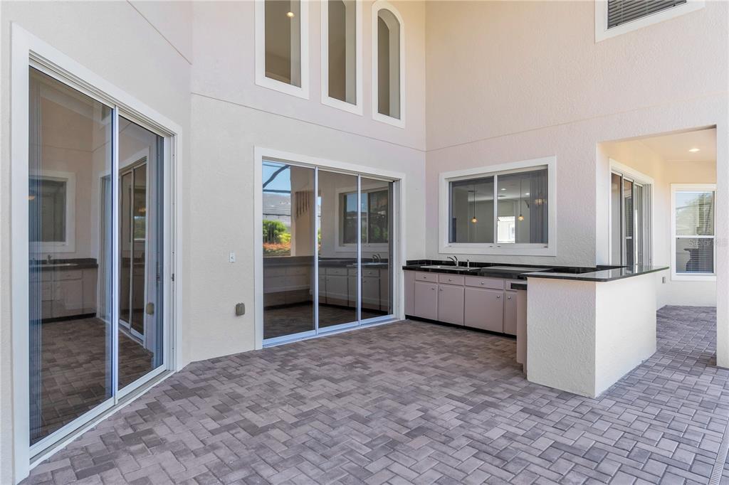 A covered patio features a brick paver floor, sliding glass doors, and an outdoor kitchen — 11538 DELWICK DRIVE, WINDERMERE, FL
