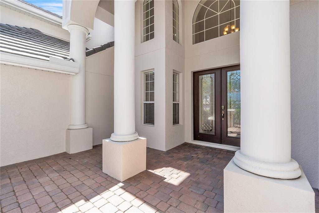 A covered entryway features a brick paver floor, white columns, and double glass-paneled front doors — 11538 DELWICK DRIVE, WINDERMERE, FL