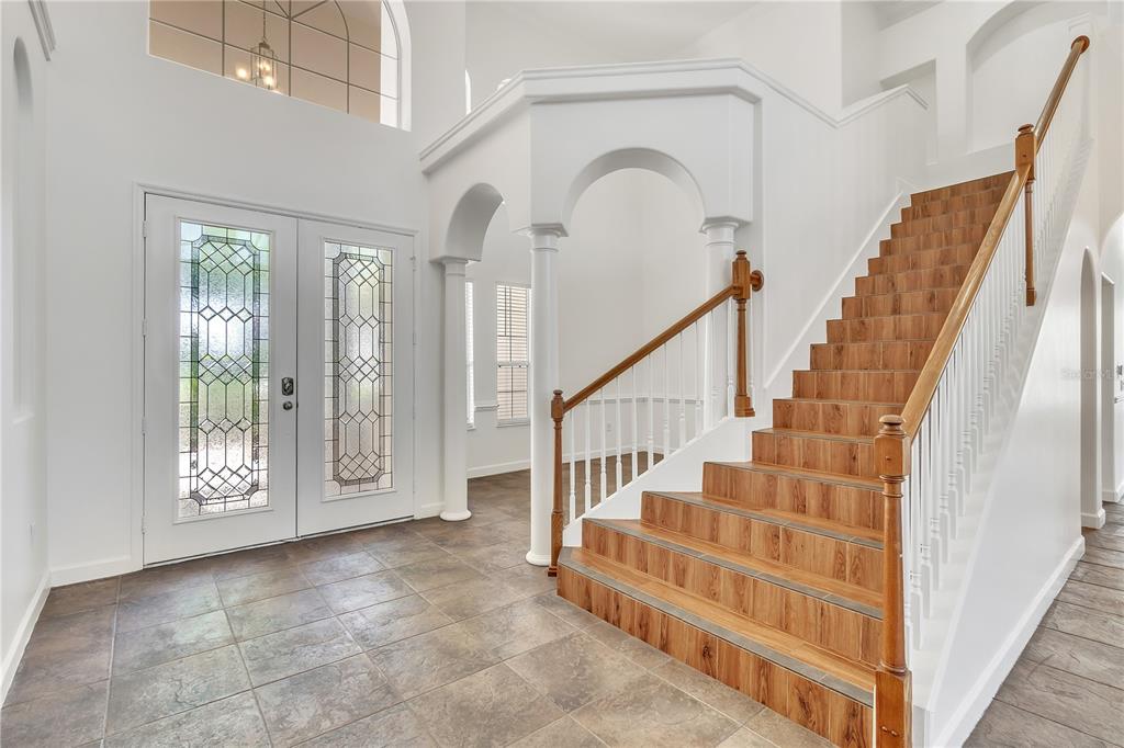 A bright foyer features a double front door, tiled floors, and a wood-tread staircase — 11538 DELWICK DRIVE, WINDERMERE, FL