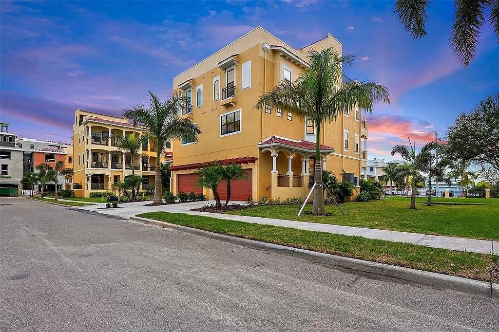 A three-story yellow stucco residential building with a two-car garage and palm trees — 6418 MARGARITA SHORES LANE, APOLLO BEACH, FL