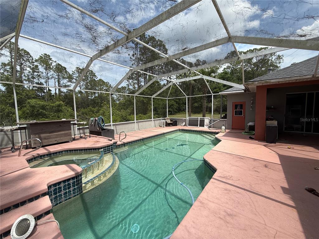 A screened-in swimming pool and spa with a red concrete deck and wooded background — 33 WENDY LANE, PALM COAST, FL