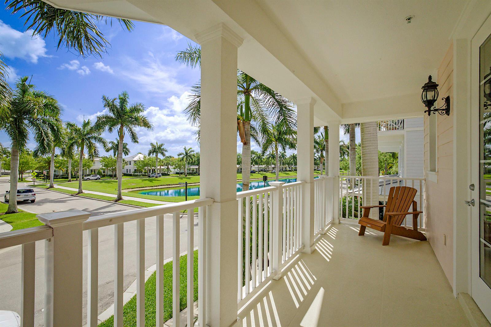 A covered balcony with white railings, a wooden chair, and a view of palm trees — 3414 W Mallory Boulevard, Jupiter FL 33458, JUPITER, FL