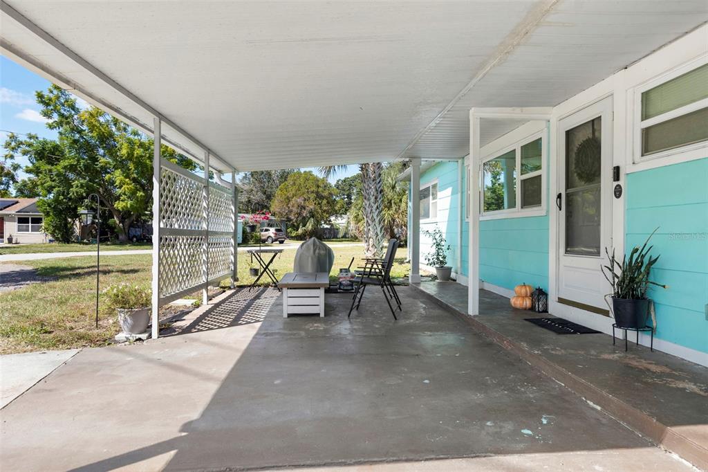 A covered concrete patio features a lattice privacy screen, outdoor furniture, and light blue siding — 7001 13TH STREET N, ST PETERSBURG, FL