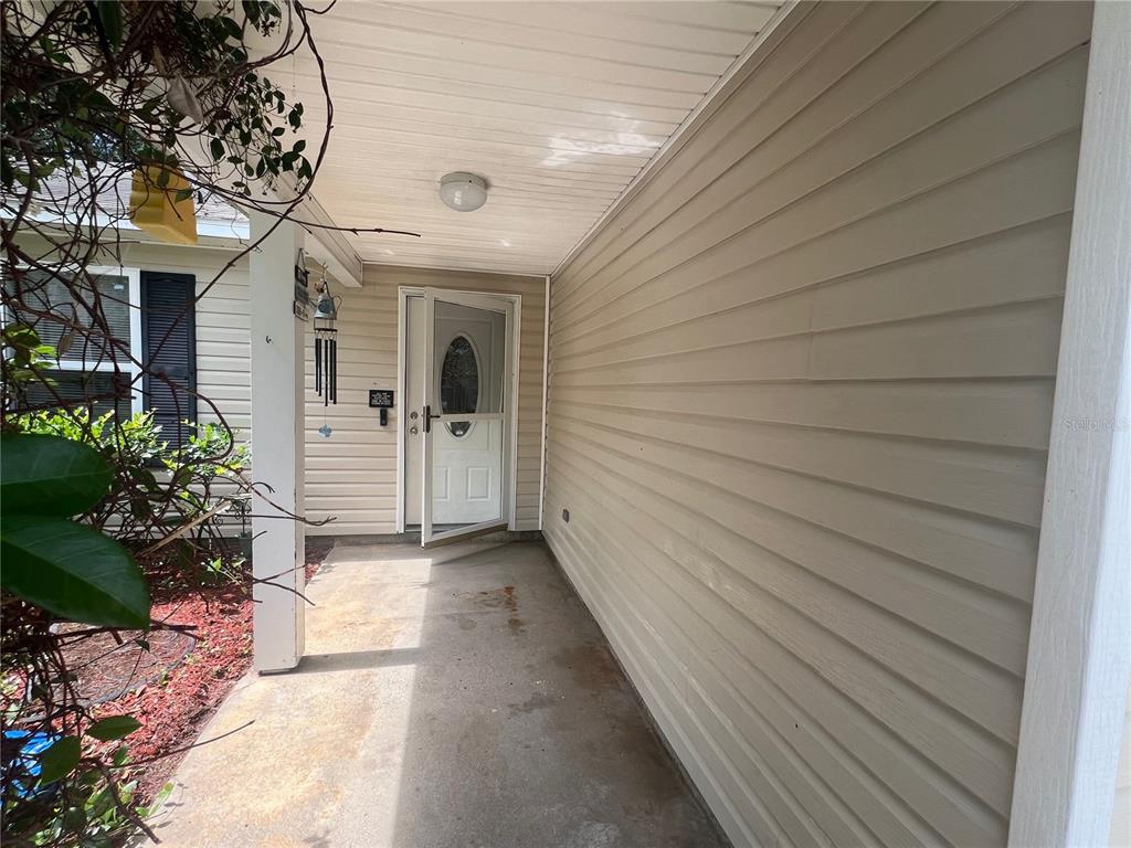 A covered concrete porch leads to a white front door with a storm door — 92 WHEATFIELD DRIVE, PALM COAST, FL