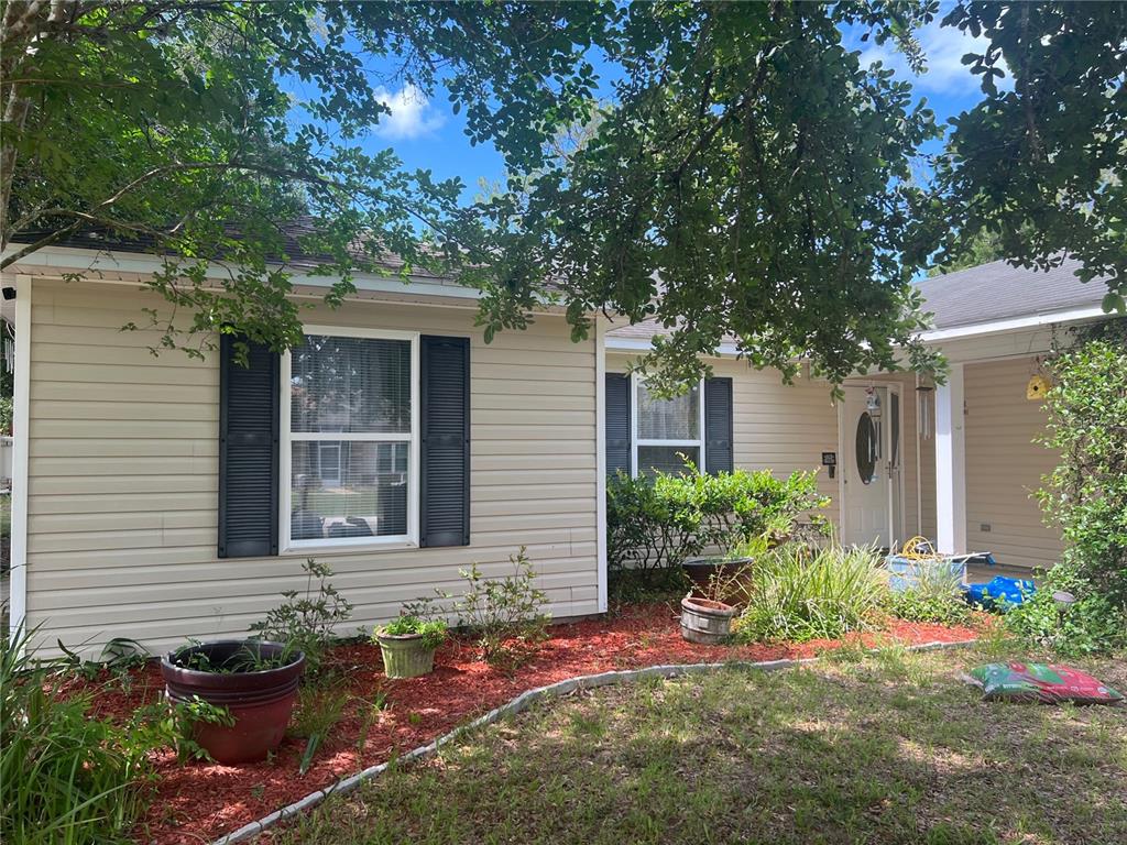 A tan vinyl-sided house features dark shutters, a front porch, and a landscaped garden bed — 92 WHEATFIELD DRIVE, PALM COAST, FL