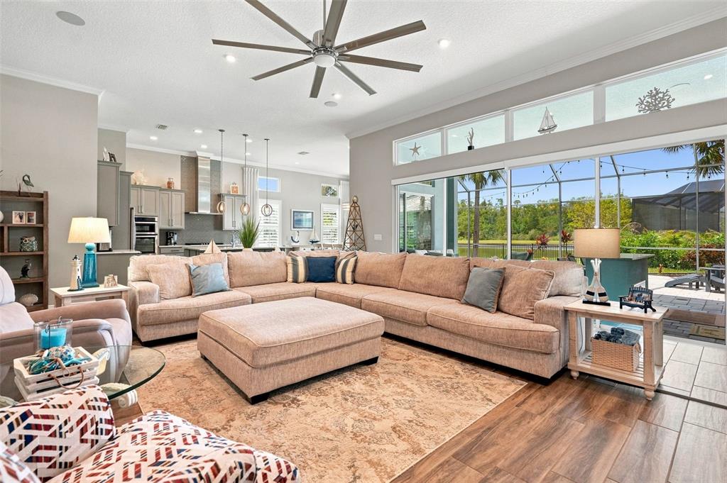 A spacious living room features a large sectional sofa, an ottoman, and sliding glass doors — 4093 EPIC COVE, LAND O LAKES, FL