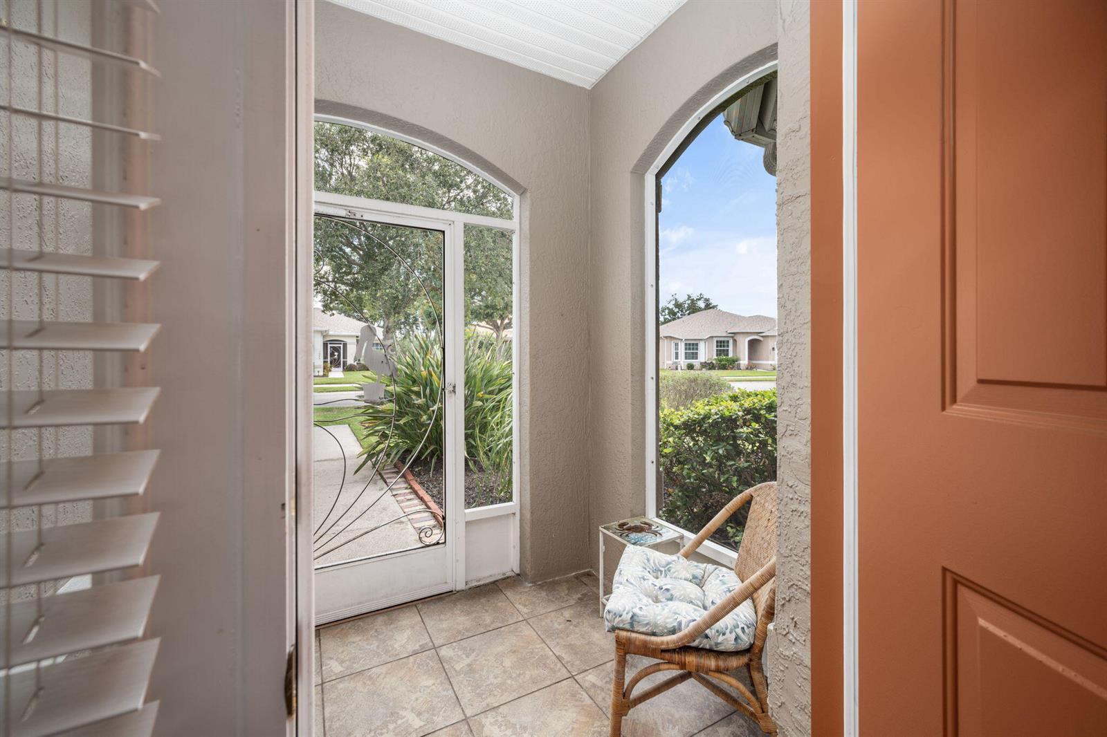 A tiled entryway features a wicker chair, a small table, and a screen door — 1336 Shoreline Circle, Sebastian FL 32958, SEBASTIAN, FL