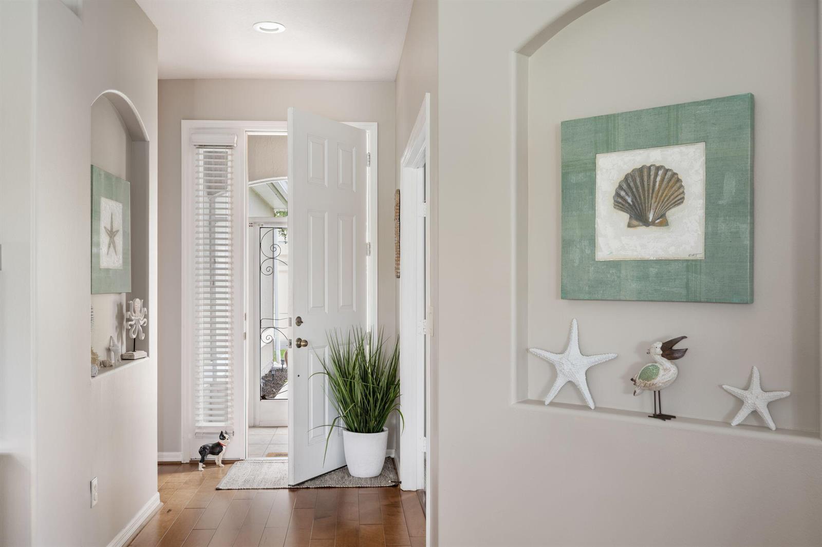 A bright entryway features hardwood floors, arched wall niches with coastal decor, and an open door — 1336 Shoreline Circle, Sebastian FL 32958, SEBASTIAN, FL