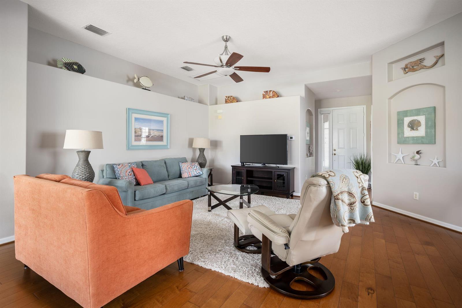 A living room features a blue sofa, orange armchair, recliner, and a television on a stand — 1336 Shoreline Circle, Sebastian FL 32958, SEBASTIAN, FL