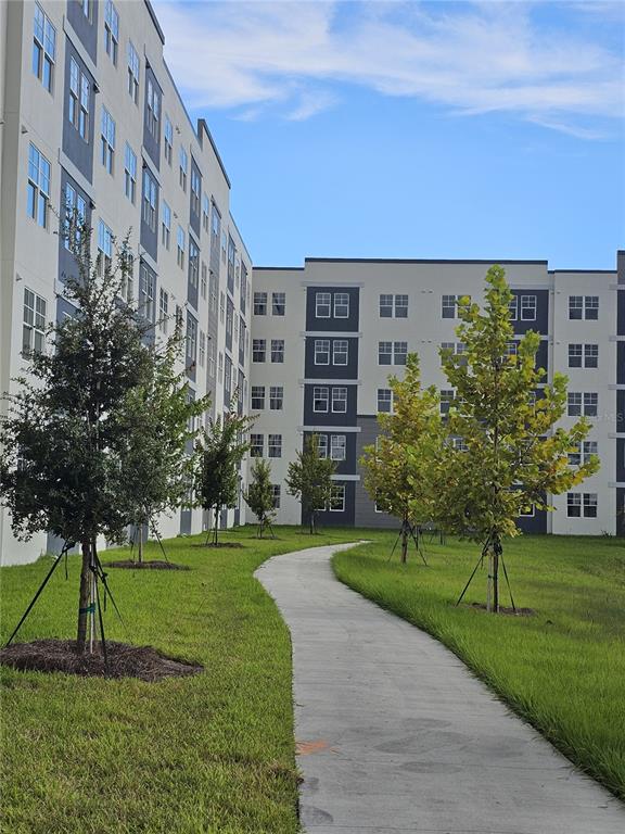A paved walkway leads between two modern apartment buildings surrounded by young trees and grass — 5579 MILLENIA PARK BOULEVARD UNIT 205, ORLANDO, FL