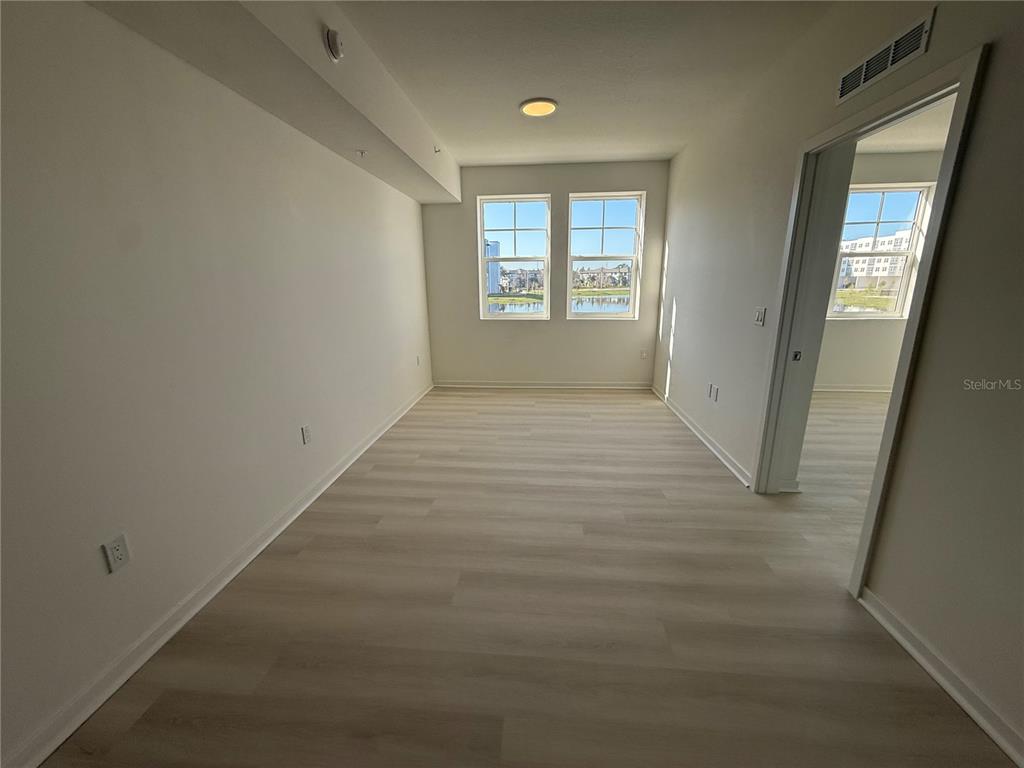 An empty room features light-colored wood-look flooring, white walls, and two windows — 5579 MILLENIA PARK BOULEVARD UNIT 205, ORLANDO, FL