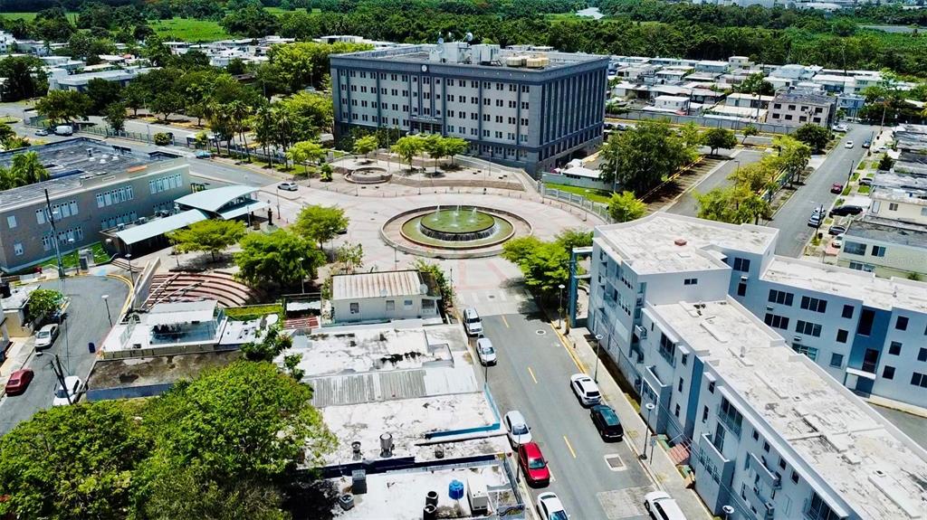 An aerial view shows a multi-story gray building, a circular fountain, and surrounding urban streets — Bo. Pueblo C. PEDRO ARZUAGA, CAROLINA, PR