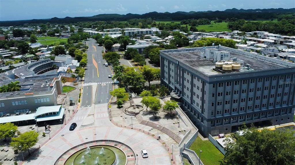 An aerial view shows a large gray building, a circular fountain, and a paved plaza — Bo. Pueblo C. PEDRO ARZUAGA, CAROLINA, PR