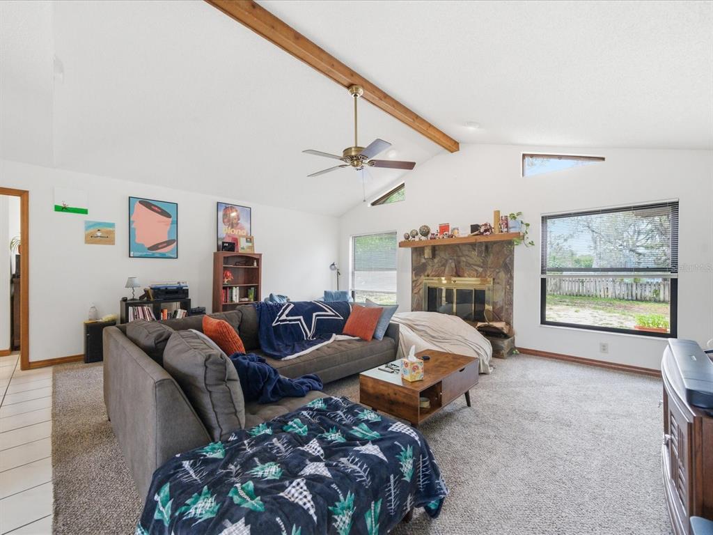 A living room features a vaulted ceiling with a wood beam, fireplace, and gray sectional — 241 DARTMOUTH AVENUE, SPRING HILL, FL