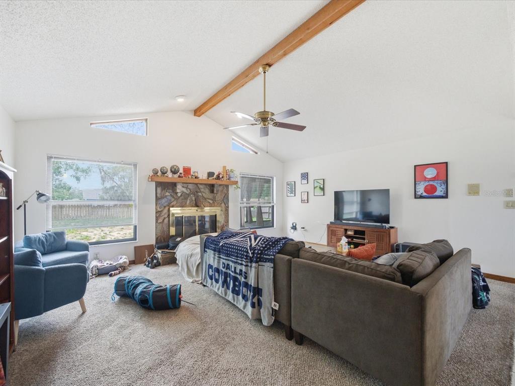 A living room features a stone fireplace, vaulted ceiling with a wood beam, and carpeted floors — 241 DARTMOUTH AVENUE, SPRING HILL, FL