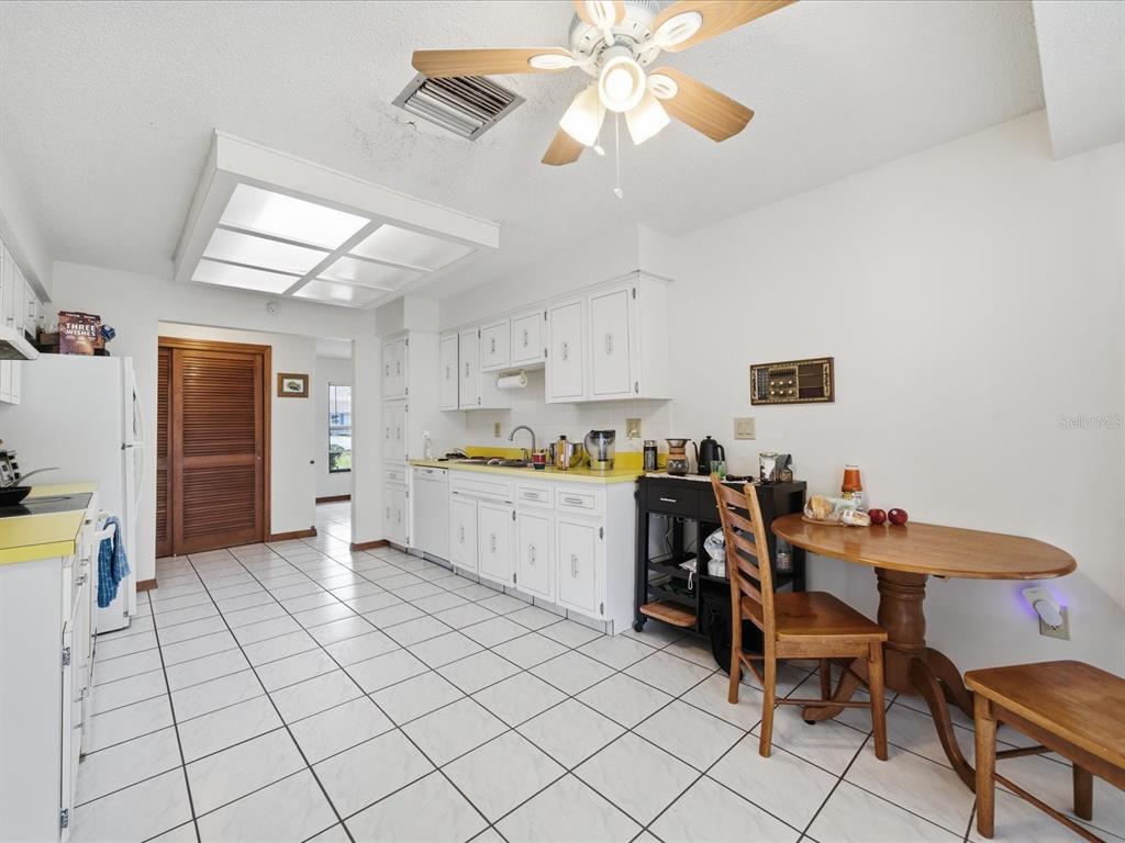 A kitchen with white cabinets, yellow countertops, white tile flooring, and a wooden dining set — 241 DARTMOUTH AVENUE, SPRING HILL, FL