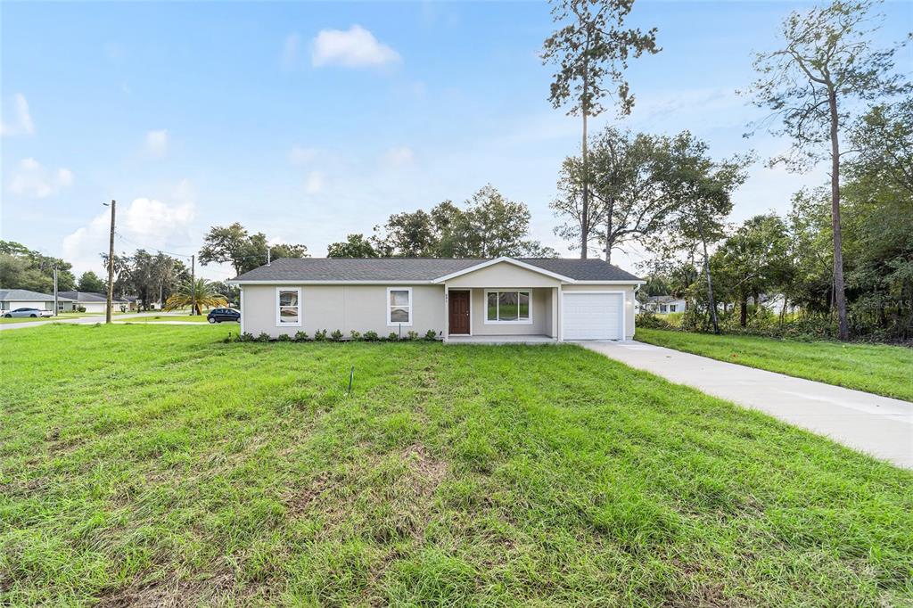 A single-story house with a light-colored exterior, a front-facing garage, and a large grassy yard — 23827 SW BEAVER DRIVE, DUNNELLON, FL