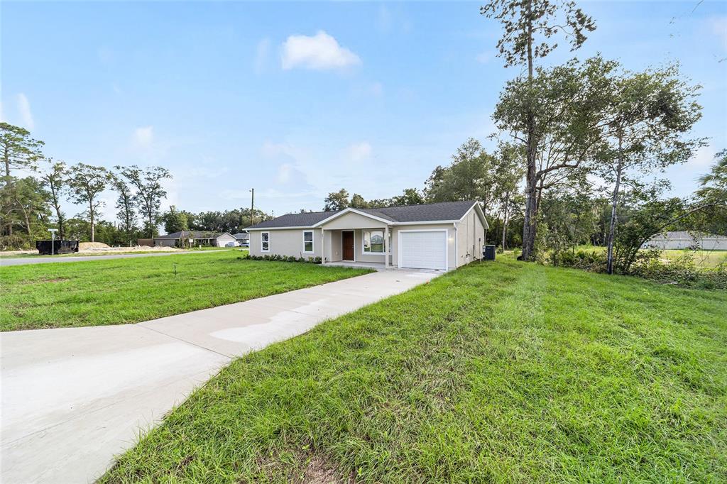 A single-story house with a white garage and concrete driveway sits on a grassy lot — 23827 SW BEAVER DRIVE, DUNNELLON, FL