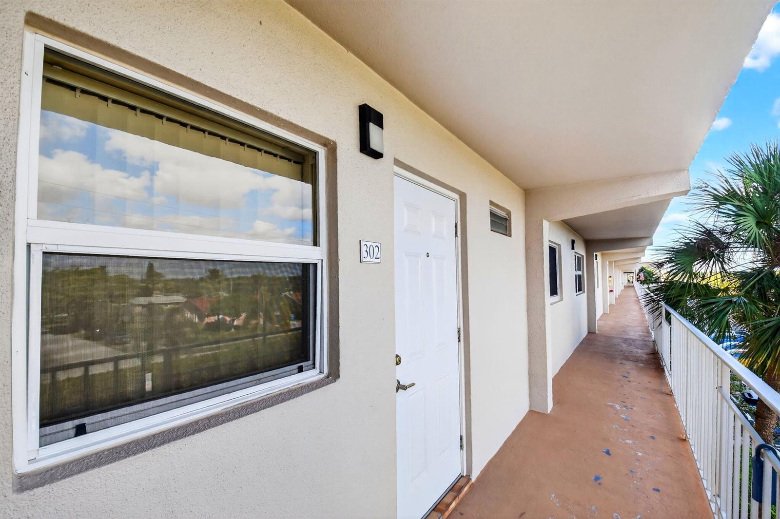 An exterior view of an apartment building hallway with a white door labeled 302 — 230 NE 26th Avenue # 3020, Boynton Beach FL 33435, BOYNTON BEACH, FL