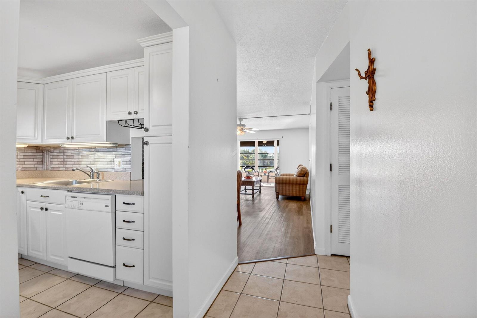 A white kitchen with tile flooring opens into a living area with wood-look floors — 230 NE 26th Avenue # 3020, Boynton Beach FL 33435, BOYNTON BEACH, FL