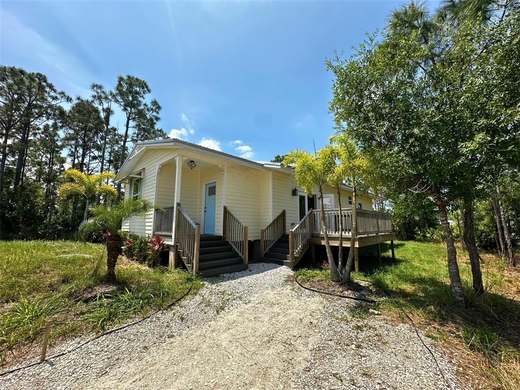 A light yellow house with a gravel driveway, wooden stairs, and a deck — 8297 STRASSE BOULEVARD, PUNTA GORDA, FL