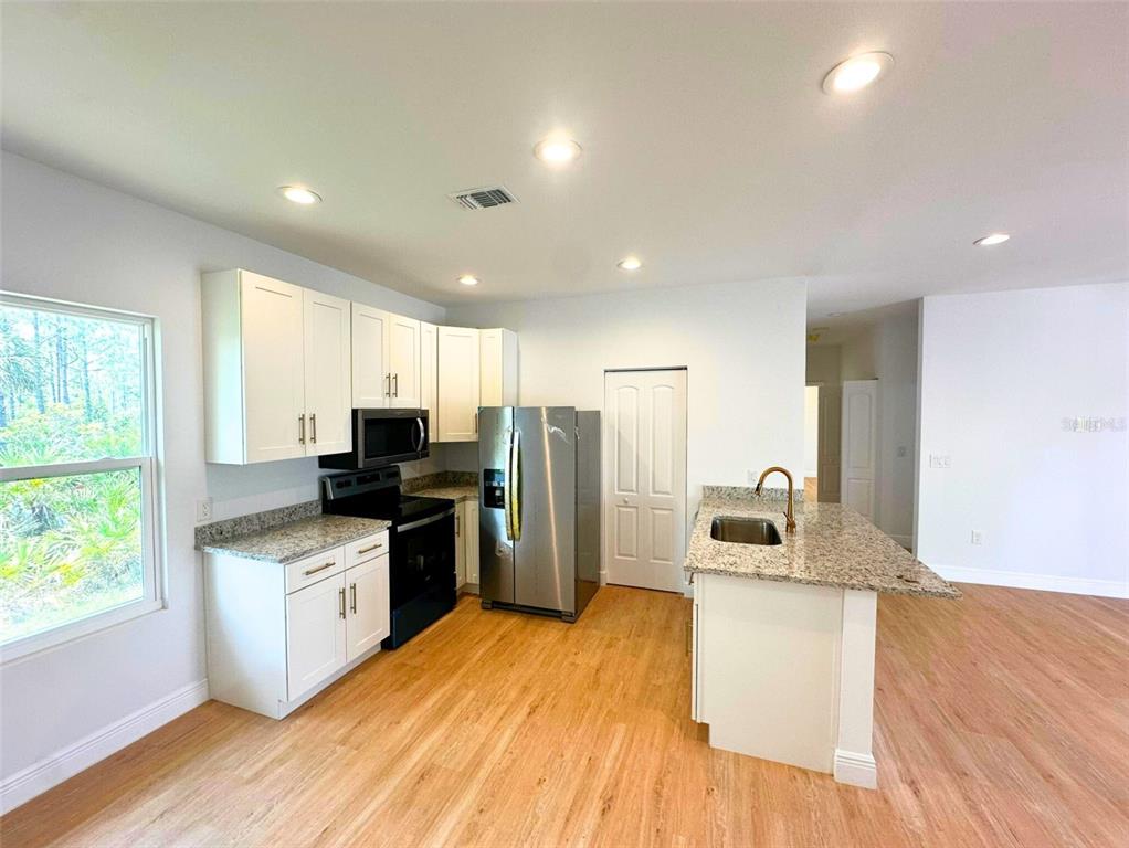 A kitchen features white cabinets, granite countertops, stainless steel appliances, and light wood-look flooring — 8297 STRASSE BOULEVARD, PUNTA GORDA, FL
