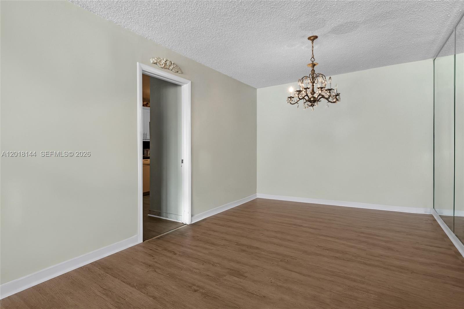 An empty room features wood-look flooring, a crystal chandelier, and a mirrored wall — 6841 SW 147th Ave # 1D, Miami FL 33193, MIAMI, FL