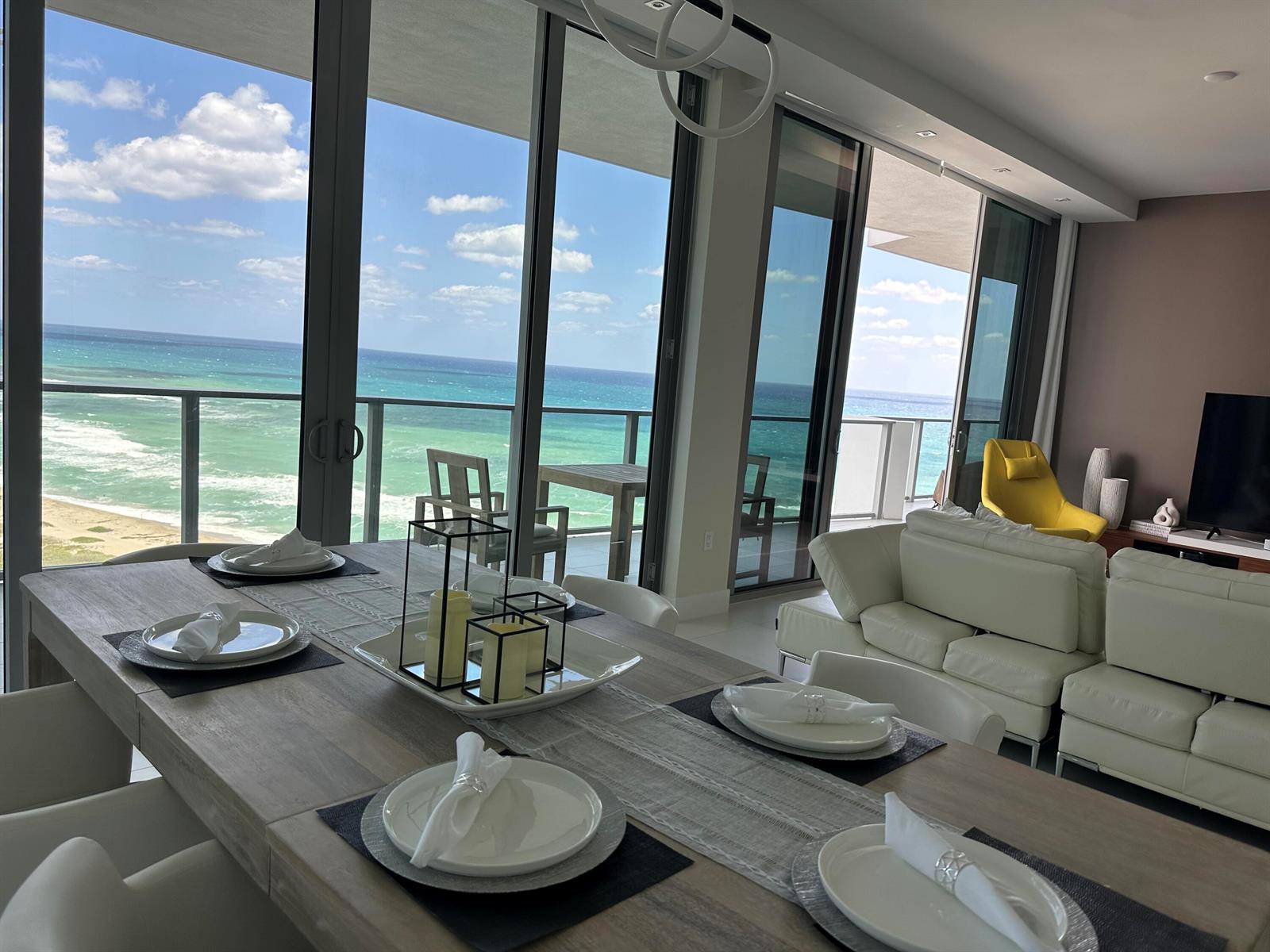 A dining area with a wooden table overlooks the ocean through large floor-to-ceiling windows — 3100 N Ocean Drive # 1701, Riviera Beach FL 33404, RIVIERA BEACH, FL