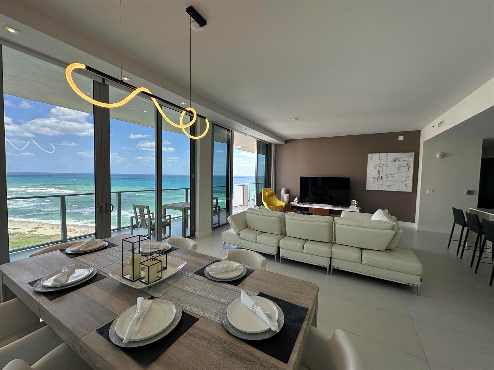 A modern living and dining area features a white sectional, ocean views, and contemporary lighting — 3100 N Ocean Drive # 1701, Riviera Beach FL 33404, RIVIERA BEACH, FL