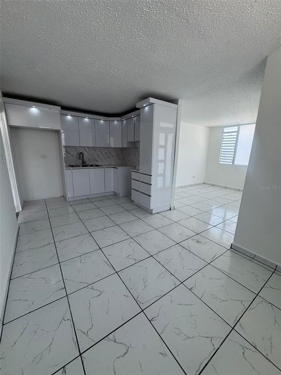 A kitchen with white cabinets and marble-patterned tile flooring opens into a living area — A-36 CALLE MARGINAL URB. BARALT, FAJARDO, PR