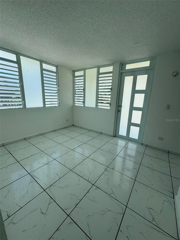 A sunroom with white marble-patterned tile flooring, louvered windows, and a modern glass-paneled door — A-36 CALLE MARGINAL URB. BARALT, FAJARDO, PR
