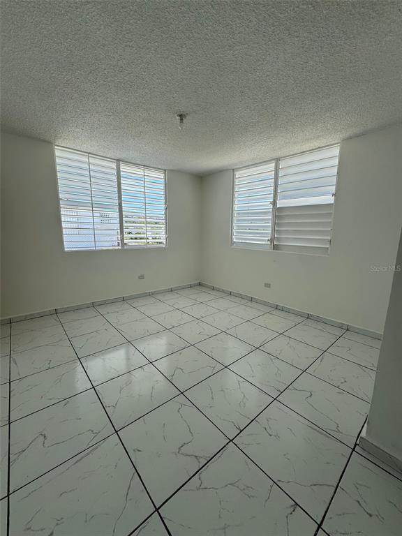 An empty room features white marble-patterned tile flooring, white walls, and louvered windows — A-36 CALLE MARGINAL URB. BARALT, FAJARDO, PR