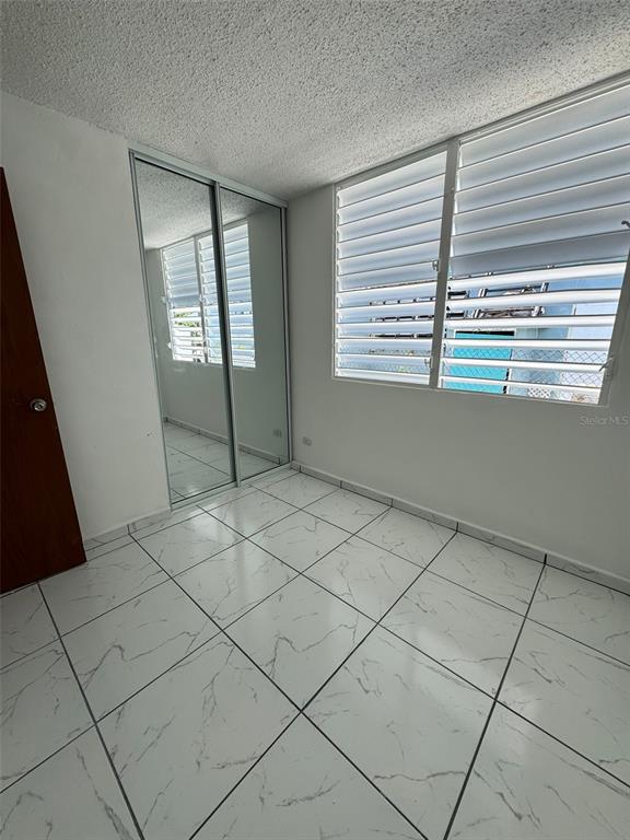 A bedroom with white marble-patterned tile floors, a mirrored closet, and louvered windows — A-36 CALLE MARGINAL URB. BARALT, FAJARDO, PR