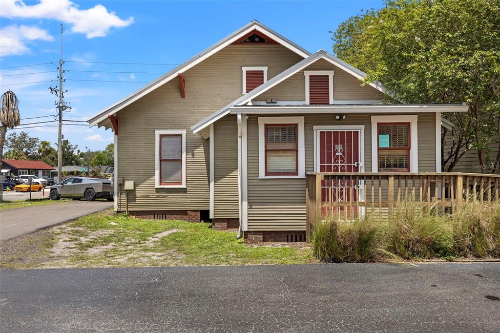 A tan, single-story house with a wooden deck and red-trimmed windows sits near a road — 5135 N FLORIDA AVENUE, TAMPA, FL