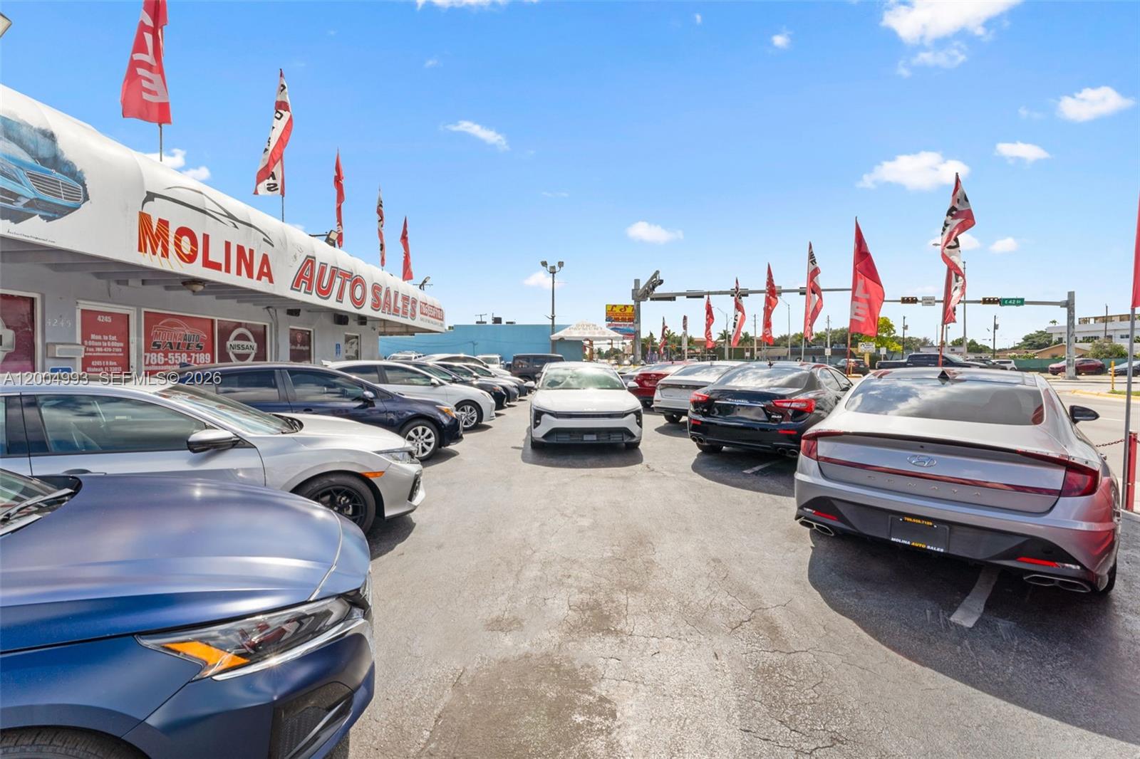 A car dealership lot features multiple parked vehicles under a bright blue sky — 10301 NW 27th Ave, Miami FL 33147, MIAMI, FL
