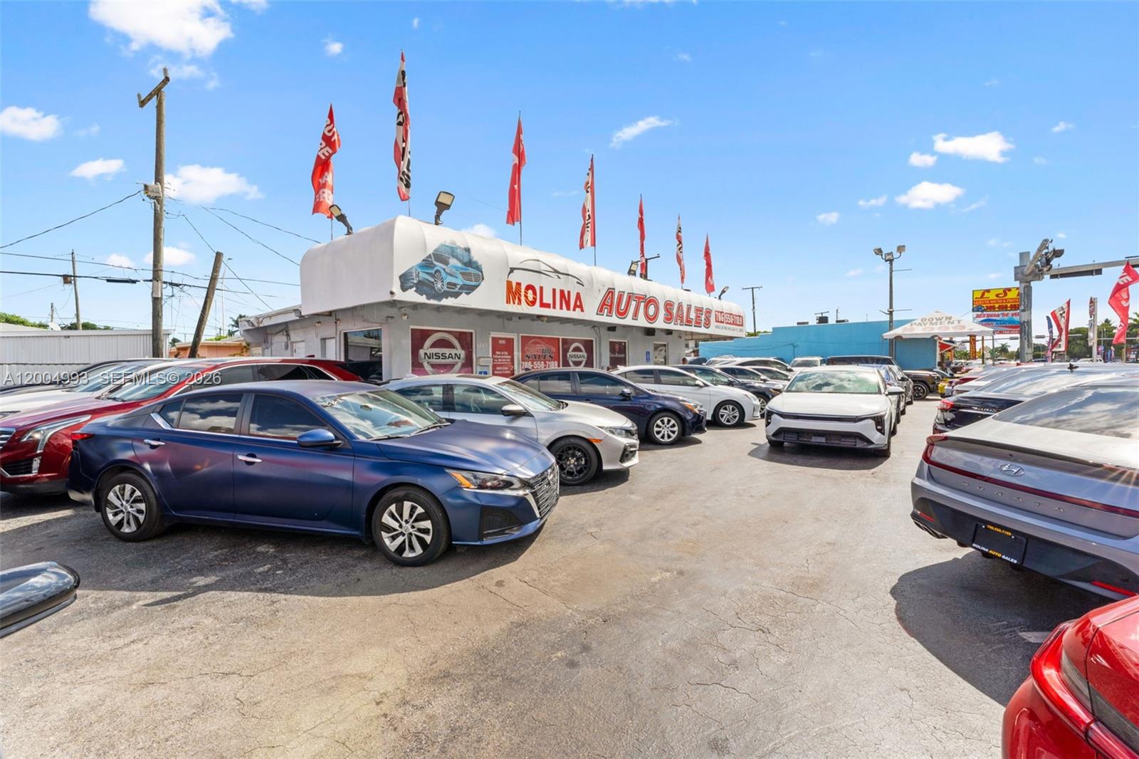 A car dealership lot features multiple parked vehicles under a branded awning and flags — 10301 NW 27th Ave, Miami FL 33147, MIAMI, FL