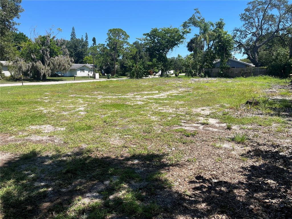 A vacant, grassy residential lot with scattered trees and surrounding houses under a clear sky — 2414 PELICAN DRIVE, SARASOTA, FL