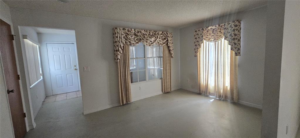 An empty living room features light-colored walls, carpeted flooring, and windows with floral valance curtains — 545 CLARK STREET, MAITLAND, FL