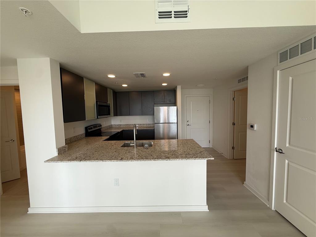 A kitchen features granite countertops, dark cabinetry, stainless steel appliances, and light-colored flooring — 5579 MILLENIA PARK BLVD UNIT 424, ORLANDO, FL