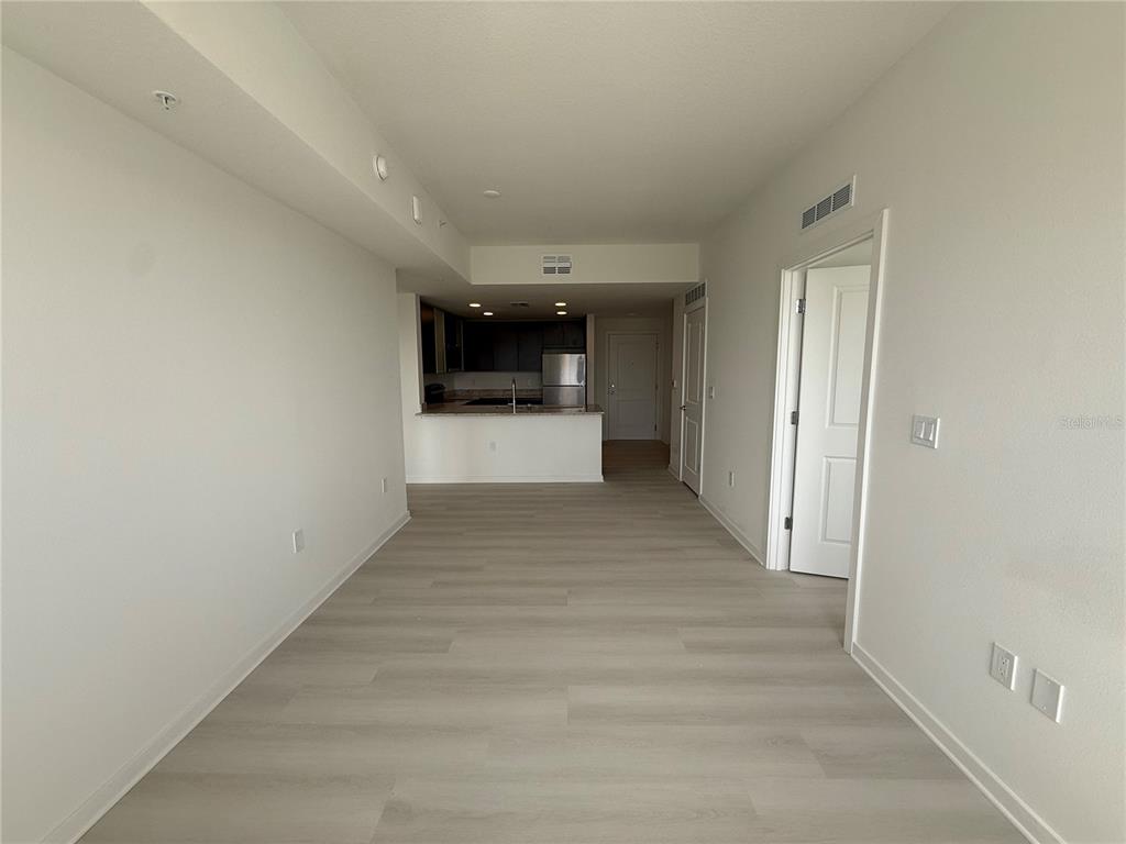 An open-concept living area features light wood-look flooring and a view into the kitchen — 5579 MILLENIA PARK BLVD UNIT 424, ORLANDO, FL