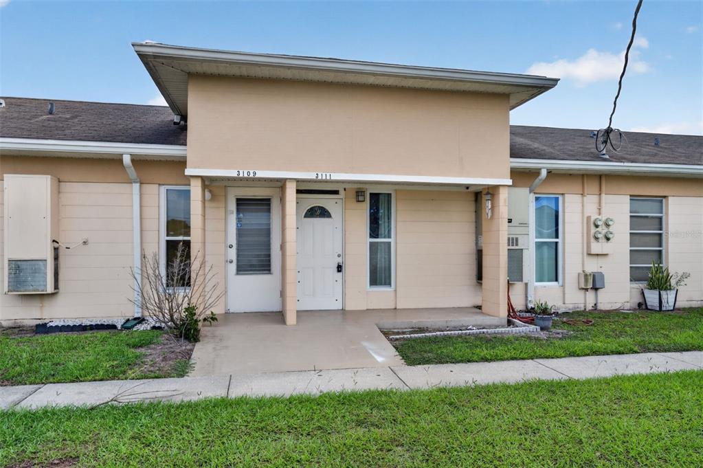 The exterior of a single-story duplex features tan siding, two front doors, and a concrete porch — 3111 CLUB CIRCLE, LAKE WALES, FL